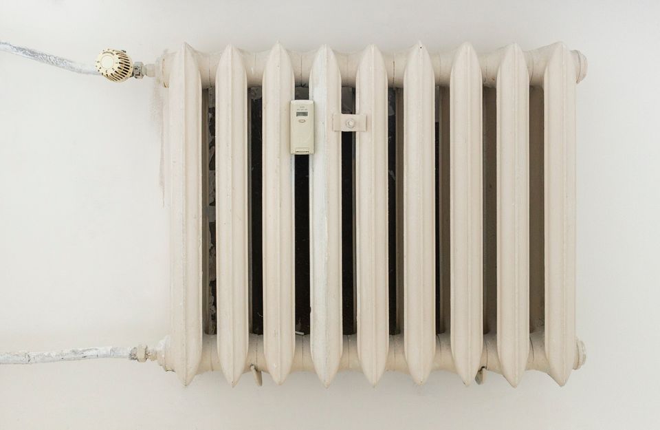 Weißer Rippenheizkörper mit Thermostat und Heizkostenverteiler an einer hellen Wand